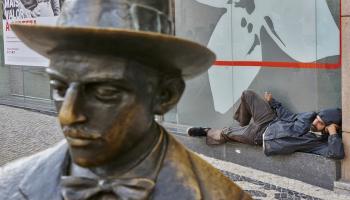رجل بلا مأوى يستريح وراء تمثال لفرناندو بيسوا في لشبونة، تشرين الأول/ أكتوبر 2020 (Getty)