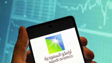 صورة تعبيرية لشعار أرامكو على هاتف ذكي مع رسم بياني لمؤشر البورصة، 19 فبراير 2023 (بودرول تشوكروت/ Getty)